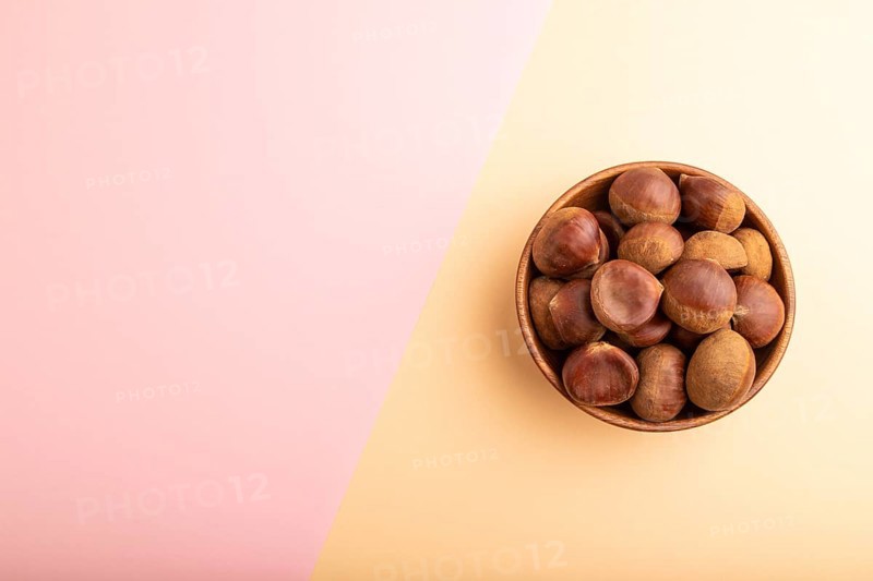 Wooden bowl with raw edible ?hestnuts on pink and orange paper pastel background, top view, flat lay, copy space, minimalism
