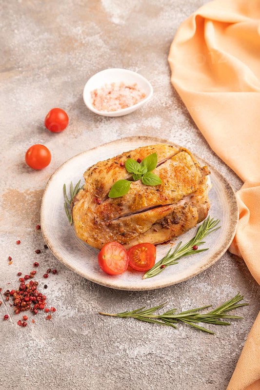 Fried Turkey Thigh with spices and rosemary on plate on brown concrete background and orange linen textile. side view, close up