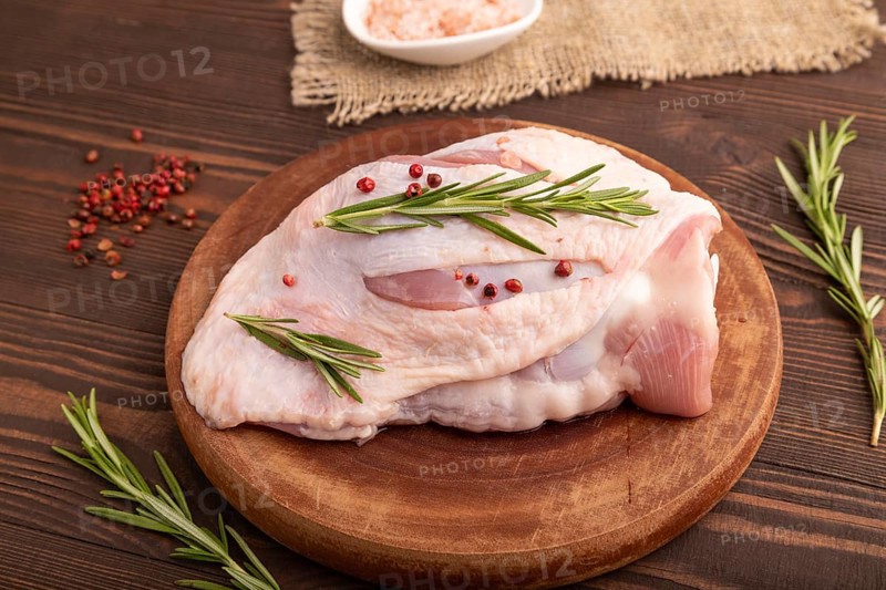Raw Turkey Thigh with spices and rosemary on cutting board on brown wooden background and linen textile. side view, close up