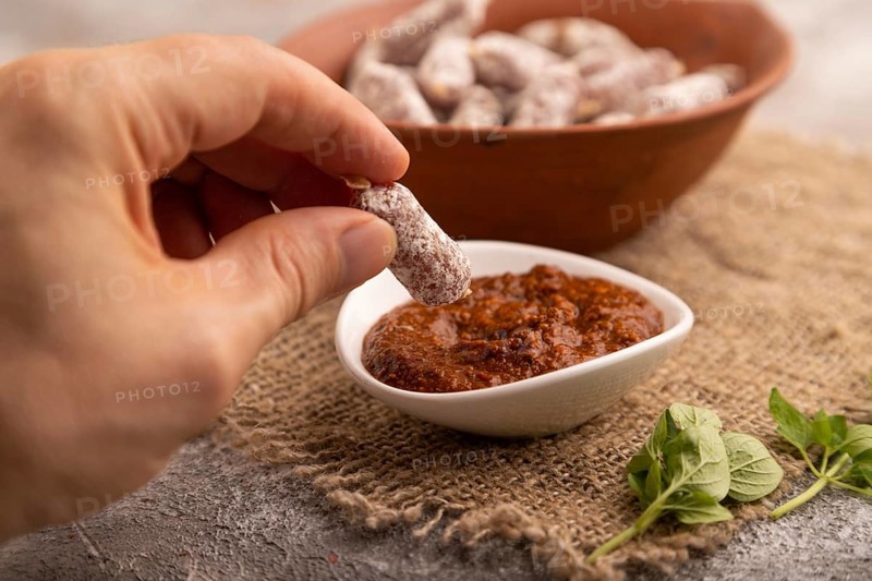 Small smoked Chicken sausages in clay bowl with hand on brown concrete background and linen textile. side view, close up, selective focus
