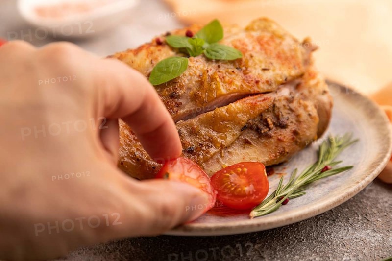Fried Turkey Thigh with spices and rosemary on plate with hand on brown concrete background and orange linen textile. side view, close up, selective focus