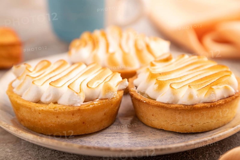 French lemon tart with meringue on brown concrete background, cup of coffee, orange linen textile, side view, close up, selective focus