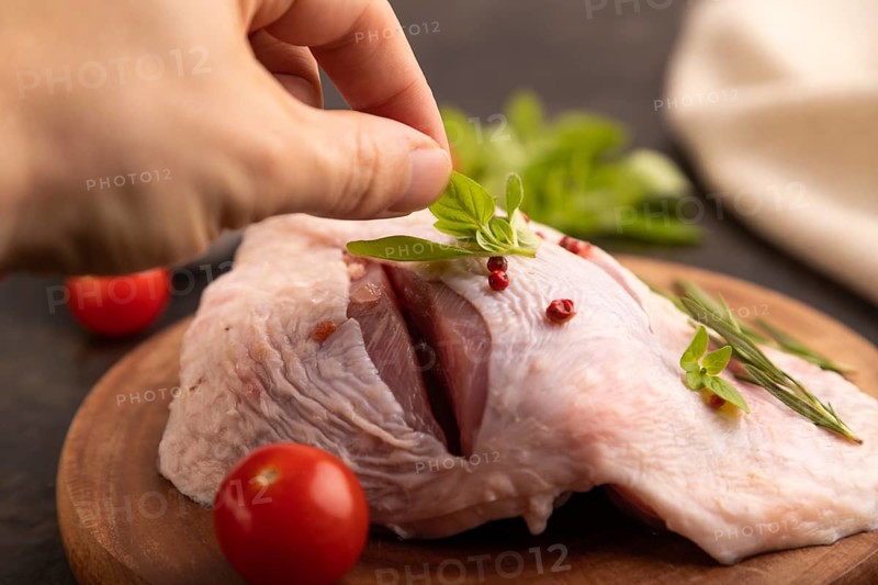 Raw Turkey Thigh with spices and rosemary on cutting board on black concrete background with hand and linen textile. side view, close up, selective focus