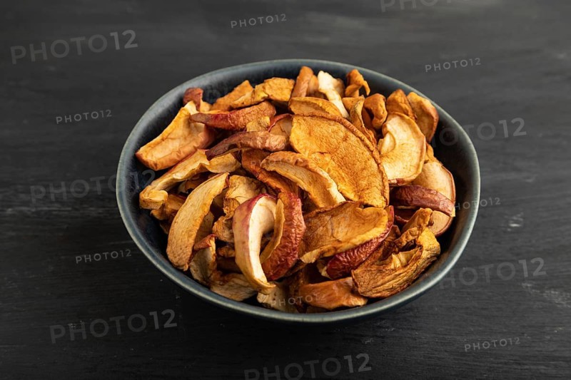 Dried Apples in ceramic bowl on black wooden background. Side view, close up. healthy food, minimalism. sweet