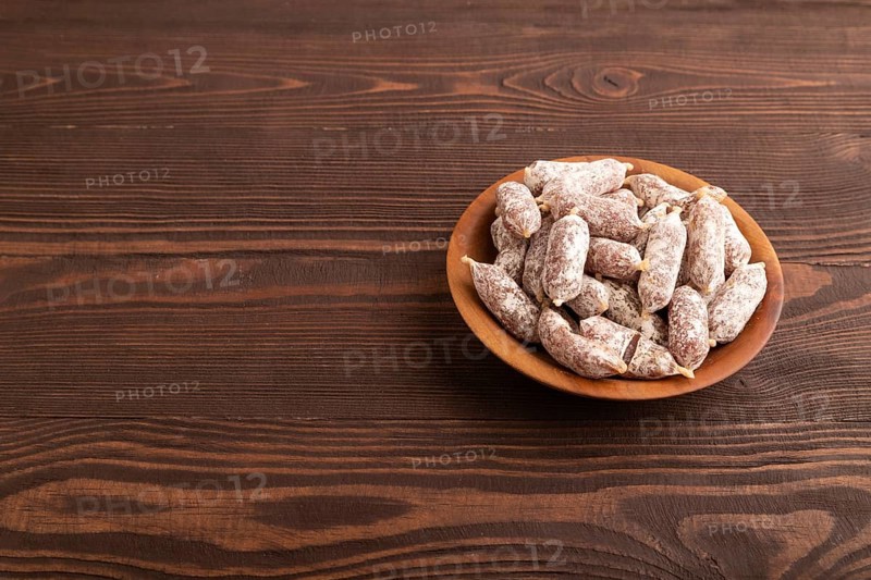 Small smoked Chicken sausages in wooden bowl on brown wooden background. side view, copy space