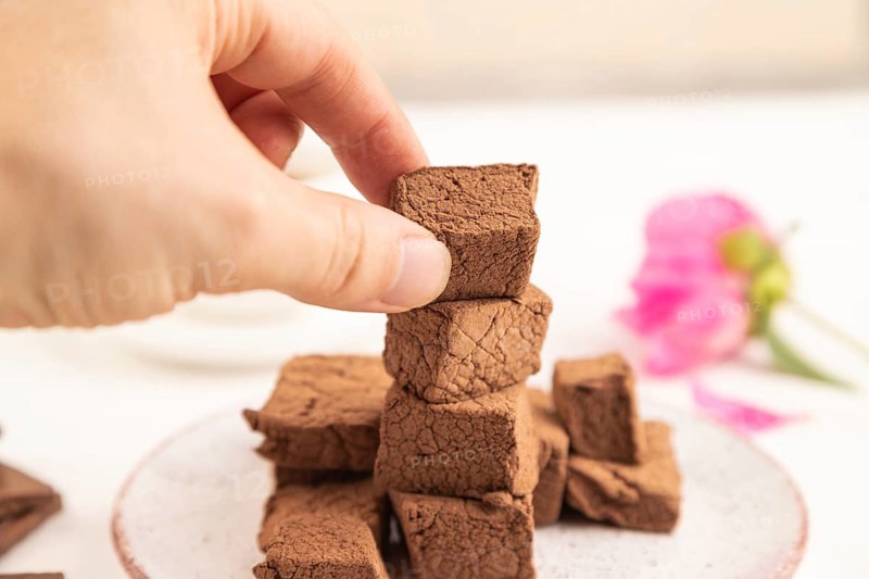 Chocolate marshmallow with cup of coffee with hand on white wooden background. side view, close up, selective focus