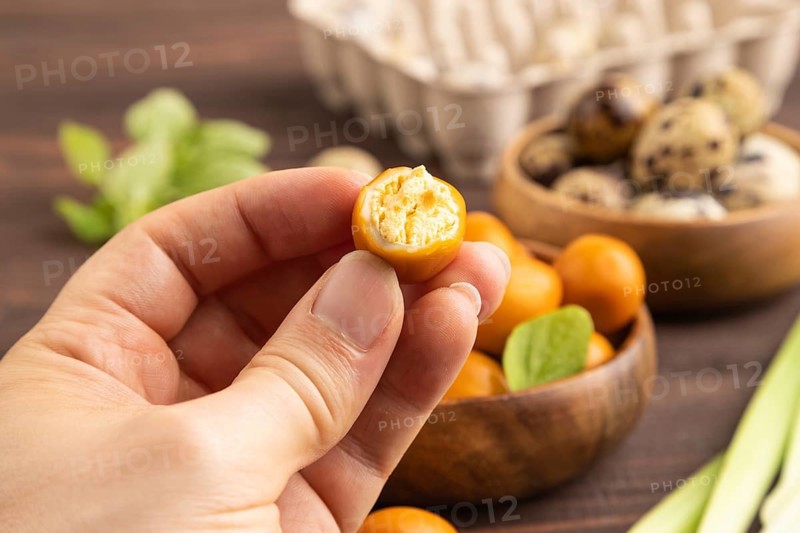 Pile of Smoked Quail eggs in bowl with hand on a brown wooden background. side view, close up, selective focus