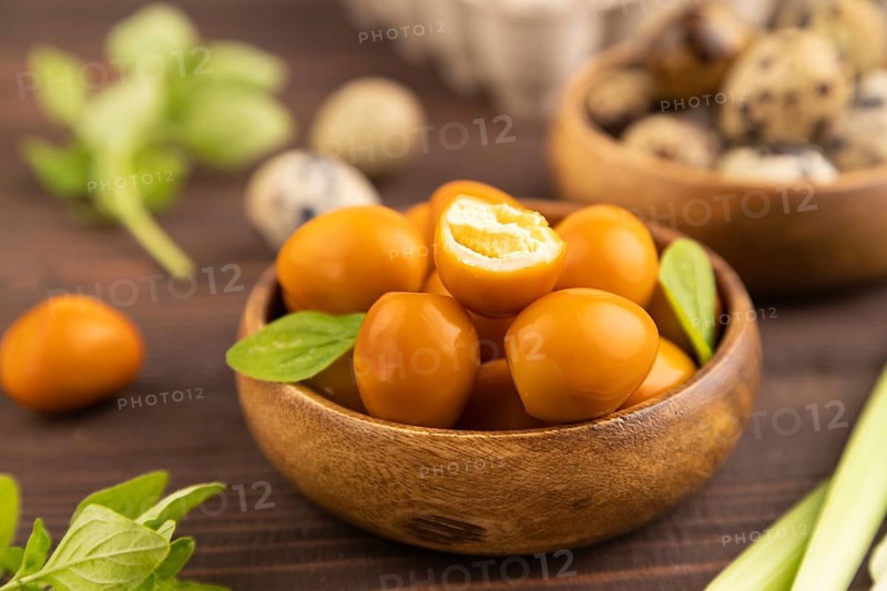 Pile of Smoked Quail eggs in bowl on a brown wooden background. side view, close up, selective focus