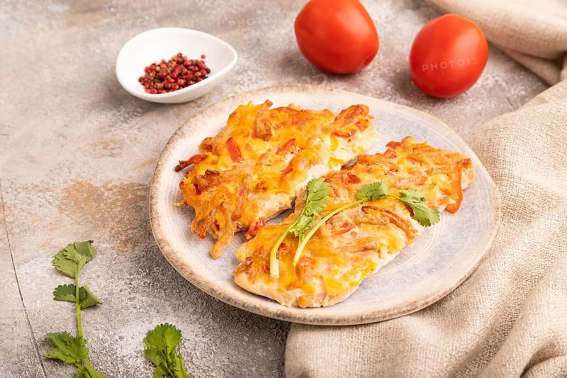 Baked chicken meat with cheese and tomatoes on brown concrete background and linen textile. side view, close up