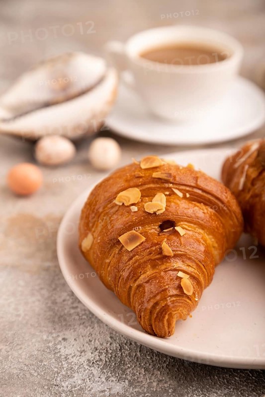 Croissant on white plate on brown concrete background and linen textile, cup of coffee, side view, close up, selective focus