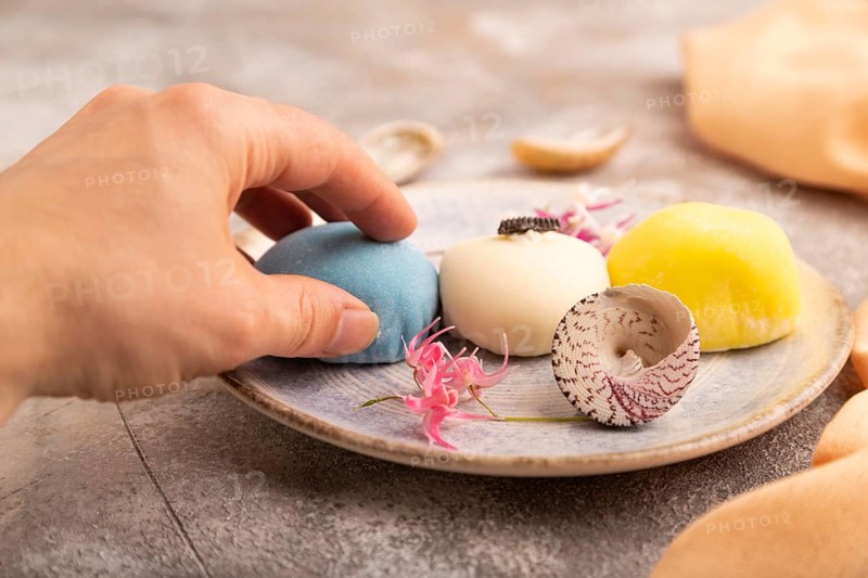 Japanese Mochi Cakes with hand on brown concrete background and orange textile, side view, close up, selective focus
