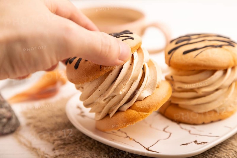 Caramel Cream Cakes with hand on white wooden background and linen textile, cup of coffee, side view, close up, selective focus