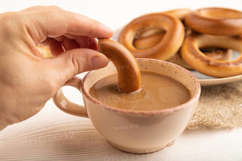 Homemade Ring Bagel with hand with cup of coffee on white wooden background and linen textile. side view, close up, selective focus