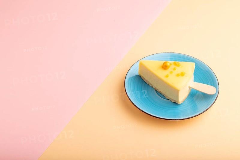 Yellow Cake pop with sprinkles on blue ceramic plate on pink and orange pastel paper background, side view, copy space, minimalism