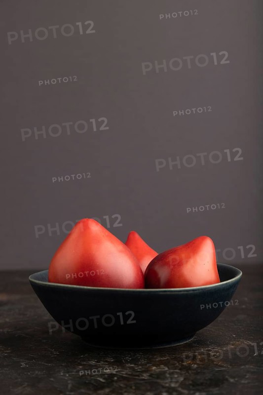 Red Heart shape tomatoes in blue bowl on black concrete background. Side view, copy space. healthy food, vegetable, minimalism, low key