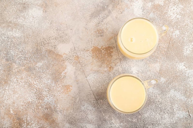 Organic non dairy banana and soy milk in glass on brown concrete background. Vegan healthy food concept, flat lay, top view, copy space