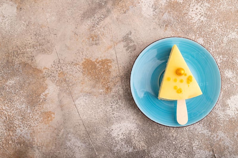 Yellow Cake pop with sprinkles on blue ceramic plate on brown concrete background, top view, flat lay, copy space, minimalism