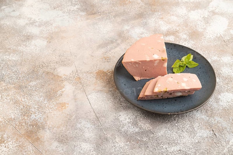 Mortadella sausage on wooden cutting board with pepper and herbs on brown concrete background. Side view, copy space