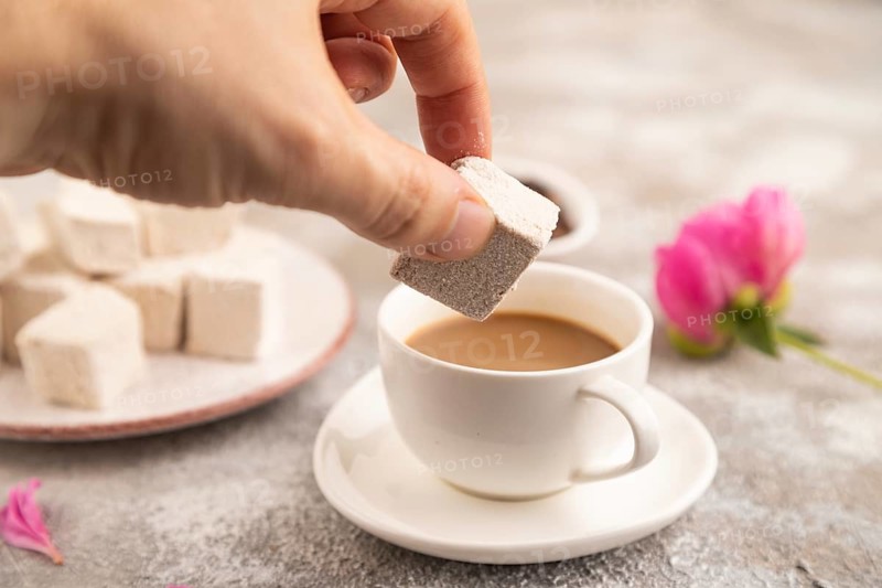 Coffee marshmallow with cup of coffee with hand on brown concrete background. side view, close up, selective focus