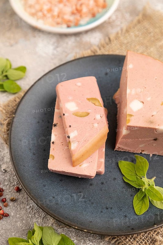 Mortadella sausage on plate with pepper and herbs on brown concrete background and linen textile. Side view, close up, selective focus