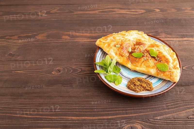 Fried homemade Khachapuri cake with cheese and meat, fried in pan. Traditional Georgian cuisine on brown wooden background. Side view, copy space
