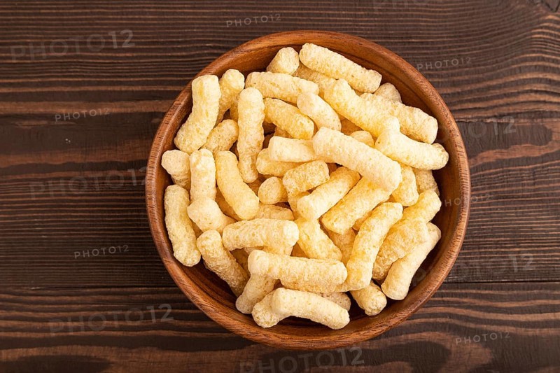 Corn flakes sticks with caramel in wooden bowl on brown wooden background. Top view, flat lay, copy space