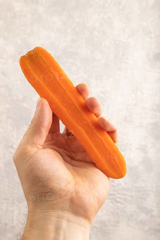 Orange Carrot with hand on gray concrete background. Top view, close up, flat lay. healthy food, vegetable, minimalism