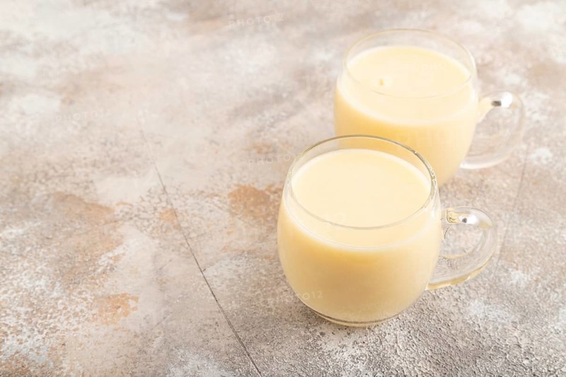 Organic non dairy banana and soy milk in glass on brown concrete background. Vegan healthy food concept, side view, copy space