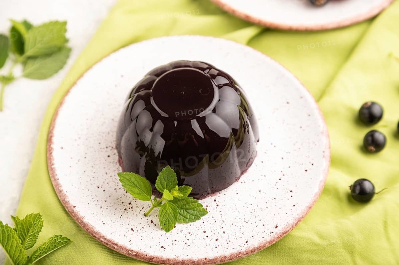 Black currant and grapes jelly on gray concrete background and green linen textile. side view, close up, selective focus