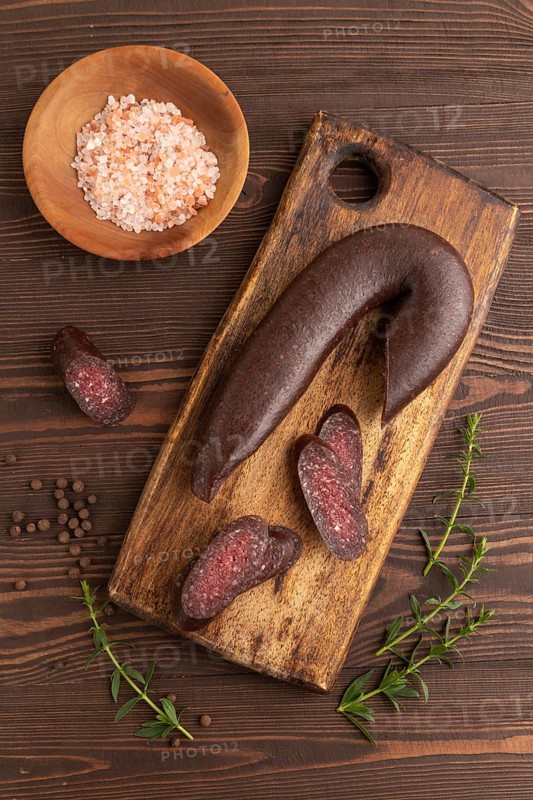 Sujuk sausage on wooden cutting board with pepper and herbs on brown wooden background. Top view, flat lay, copy space