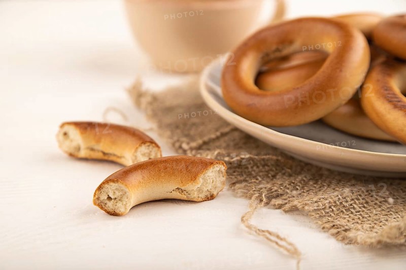 Homemade Ring Bagel with cup of coffee on white wooden background and linen textile. side view, close up, selective focus