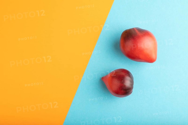 Red Heart shape tomatoes on blue and orange pastel paper background. Top view, copy space, flat lay. healthy food, vegetable, minimalism