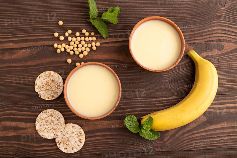 Organic non dairy banana and soy milk in clay cup on brown wooden background. Vegan healthy food concept, flat lay, top view, close up