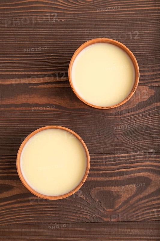 Organic non dairy banana and soy milk in clay cup on brown wooden background. Vegan healthy food concept, flat lay, top view, close up