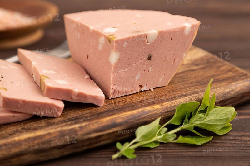 Mortadella sausage on wooden cutting board with pepper and herbs on brown wooden background. Side view, close up, selective focus