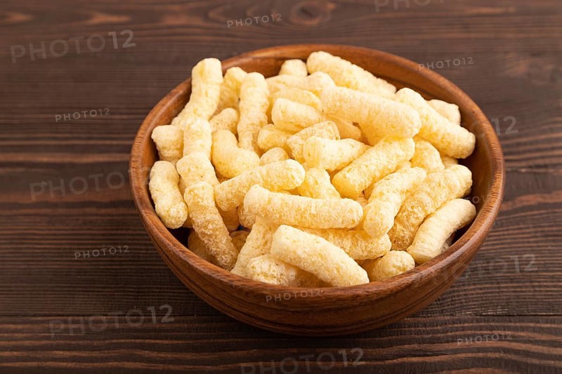 Corn flakes sticks with caramel in wooden bowl on brown wooden background. side view, close up