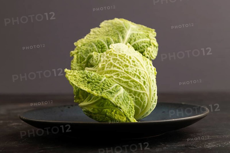 Green lettuce on blue plate on black concrete background. Side view, copy space. healthy food, vegetable, minimalism, low key