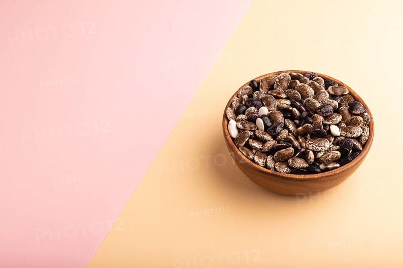 Wooden bowl with Kidney beans on pink and orange pastel paper background, side view, copy space, minimalism
