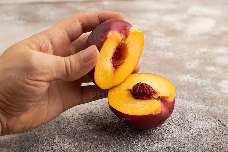Peach Cut in half with hand on brown concrete background. Side view, copy space. healthy food, vegetable, minimalism