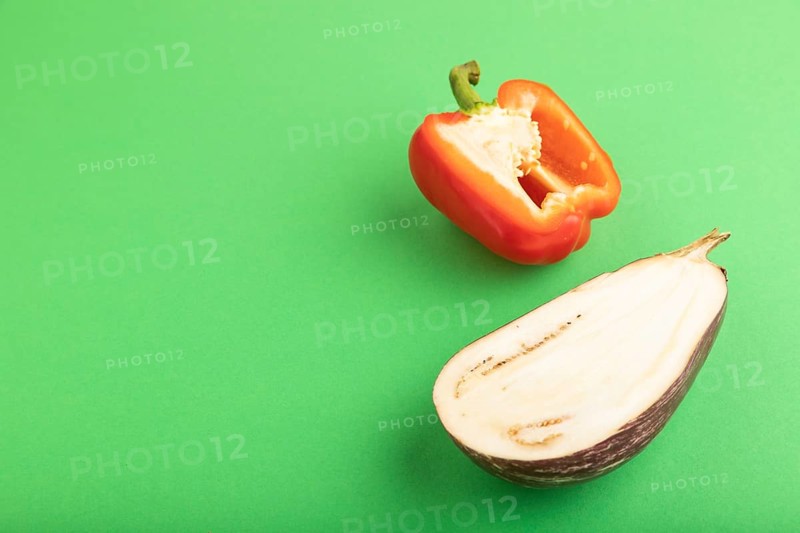 Red Cutted pepper and Purple Cutted eggplant on green pastel background. Side view, copy space. Tropical, healthy food, vegetable, slice, minimalism