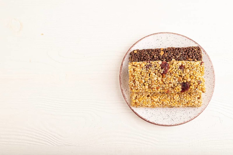 Granola bars with caramel, nuts, flakes in ceramic plate on white wooden background. Top view, flat lay, copy space