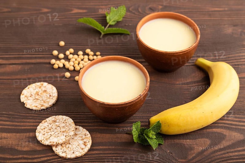 Organic non dairy banana and soy milk in clay cup on brown wooden background. Vegan healthy food concept, flat lay, side view, close up