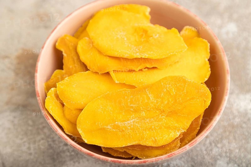 Dried Mango in ceramic bowl on brown concrete background. Side view, close up, selective focus. healthy food, minimalism