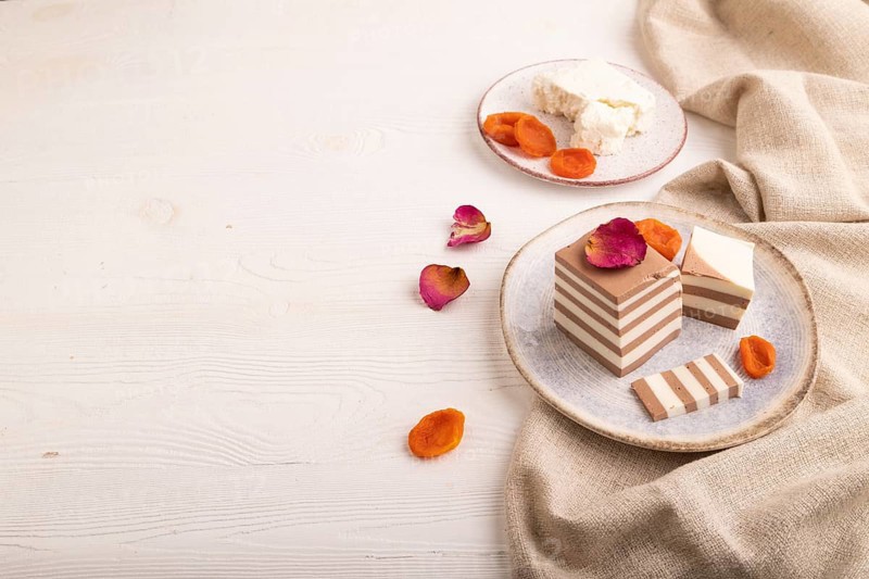 Cocoa and milk jelly with dried apricots on white wooden background and linen textile, side view, copy space, minimalism