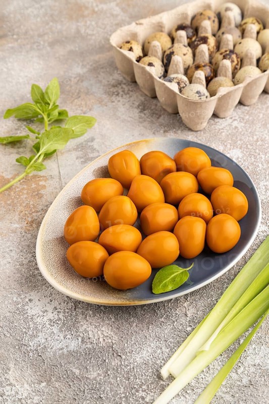 Pile of Smoked Quail eggs on plate on a brown concrete background. side view, close up
