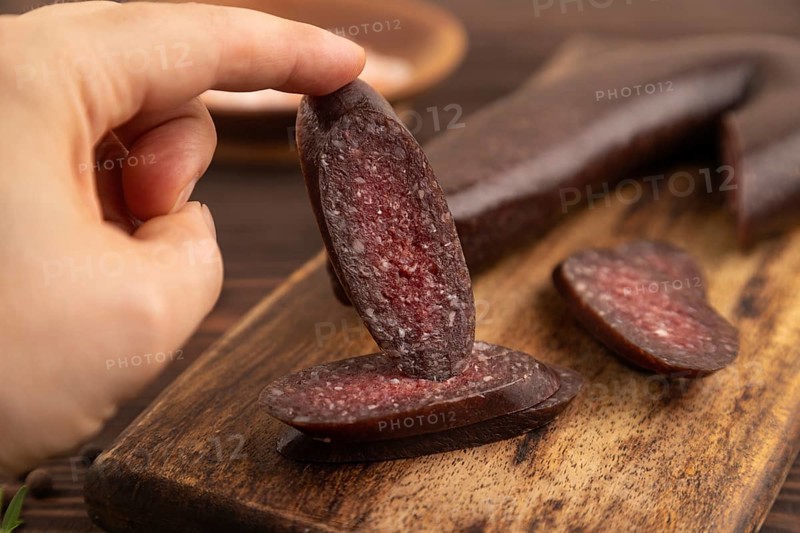 Sujuk sausage with hand on wooden cutting board with pepper and herbs on brown wooden background. Side view, close up, selective focus