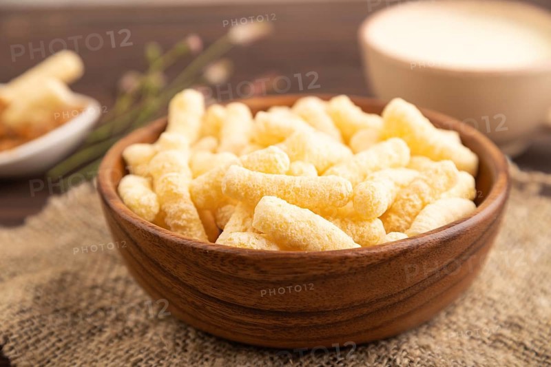 Corn flakes sticks with caramel in wooden bowl on brown wooden background and linen textile. Side view, close up, selective focus