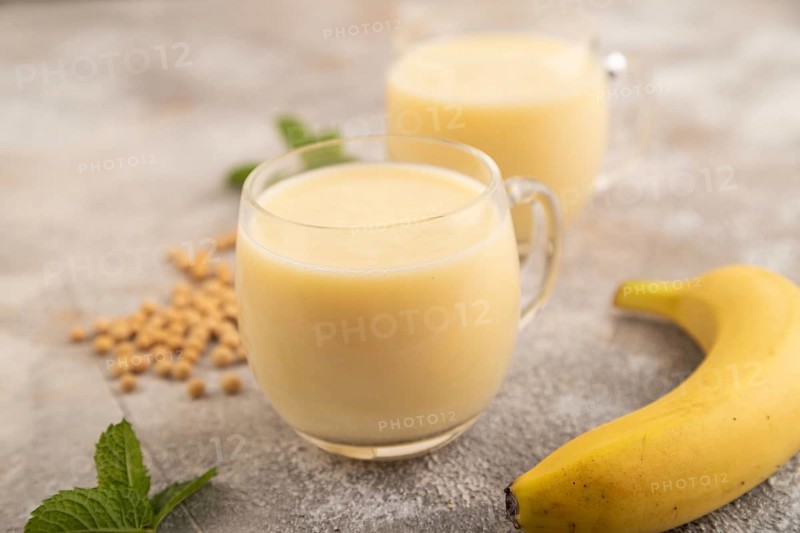 Organic non dairy banana and soy milk in glass on brown concrete background. Vegan healthy food concept, side view, close up, selective focus