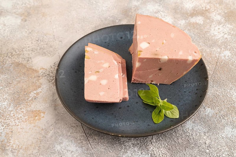 Mortadella sausage on wooden cutting board with pepper and herbs on brown concrete background. Side view, copy space