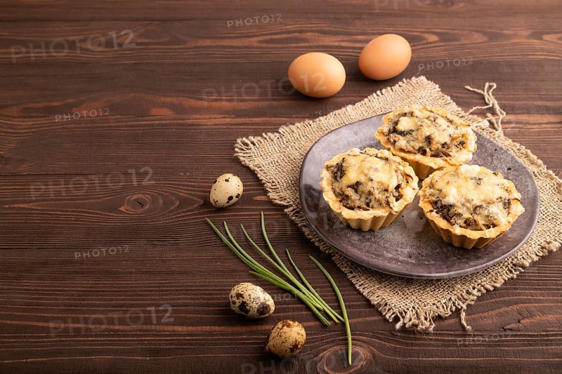 Tartlets with meat and cheese on brown wooden background and linen textile. side view, copy space